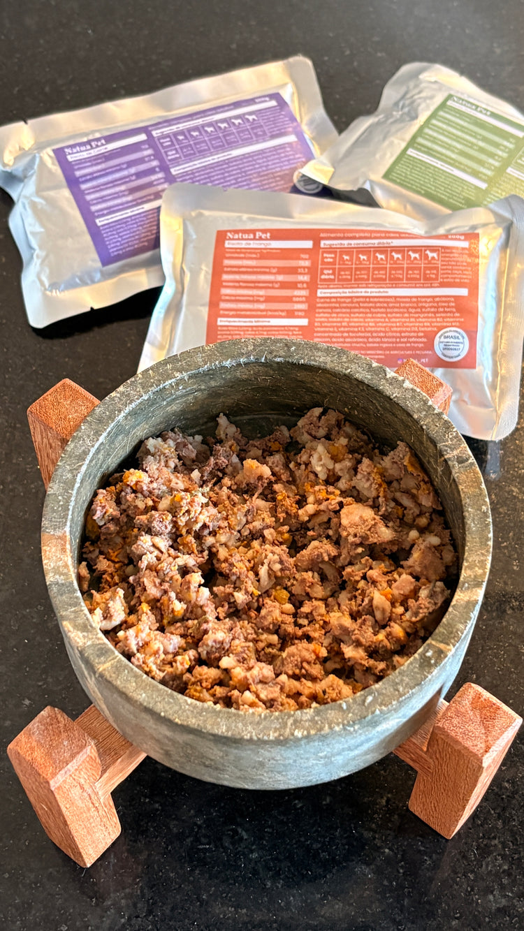 Pote com comida natural Natua Pet servida, com os sachês ao fundo